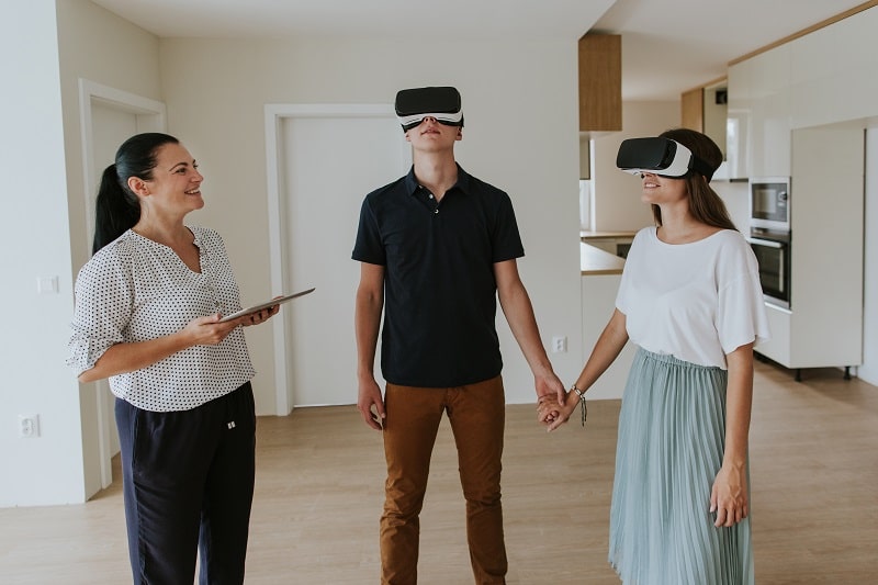 Estate agent with young couple wearing VR headsets in new apartment